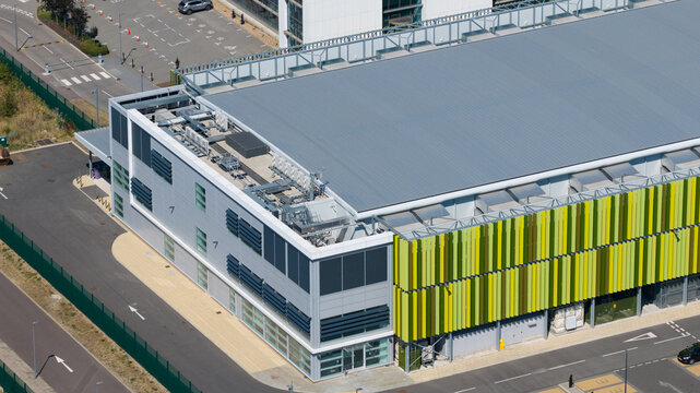 Aerial view of the Kao Data facility with green and yellow vertical louvers, a flat roof with HVAC units, and surrounding paved areas in Harlow, England, United Kingdom.