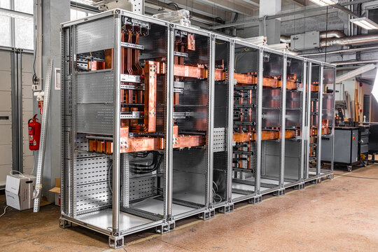 View of a large industrial electrical switchgear cabinet featuring intricate copper busbars and a modular metal frame in a workshop setting in Latvia.