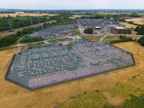 Aerial view of Staythorpe Power Station electrical substation with complex metal infrastructure and high-voltage power lines surrounded by rural fields in Staythorpe, England, United Kingdom.