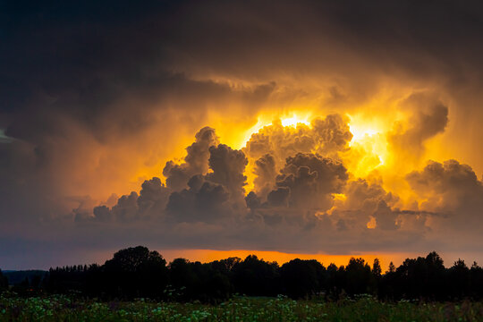 View of dramatic storm clouds illuminated by a golden sunset over the rural landscape of Latvia.