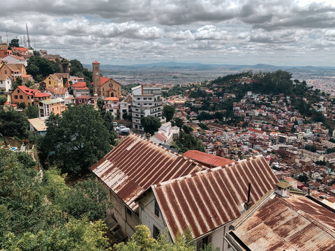 Madagascar - 23 November 2023: View of Antananarivo with its dense hillside urban landscape, historic church, and rusty corrugated metal roofs under a cloudy sky.