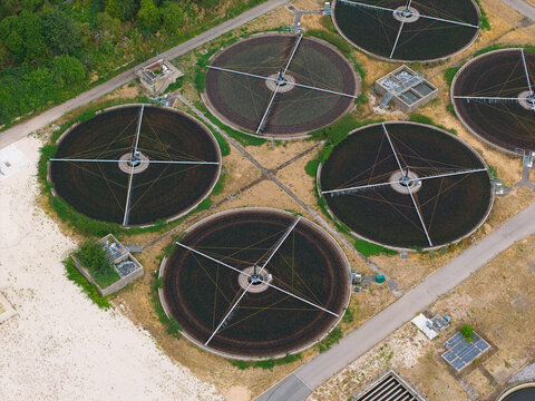 Aerial view of a sewage treatment plant featuring large circular filtration tanks with rotating mechanical arms, surrounded by pathways and vegetation in Rainworth, England, United Kingdom.