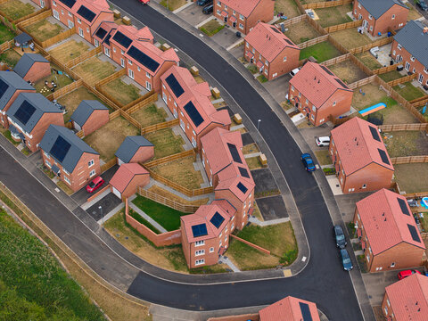 Aerial view of a residential new build suburb with modern brick houses, solar panels on rooftops, and winding roads in Burton upon Trent, England, United Kingdom.