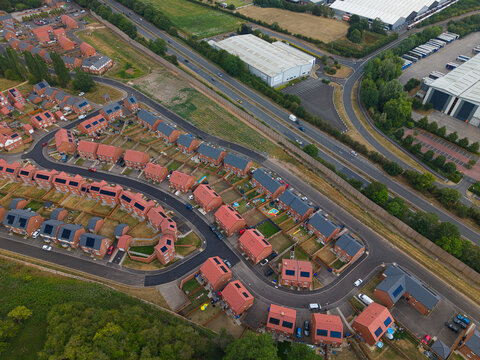 Aerial view of a modern residential new build suburb with rows of red brick houses, solar panels on rooftops, and manicured gardens in Burton upon Trent, England, United Kingdom.
