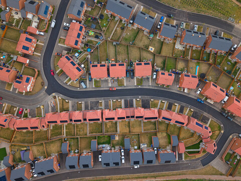 Aerial view of residential new build suburb with rows of modern houses featuring solar panels and private gardens along curved streets in Burton upon Trent, England, United Kingdom.