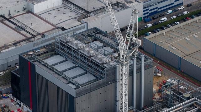 Aerial view of a modern data center building under construction with a large white crane on the rooftop and industrial infrastructure in Slough, England, United Kingdom.