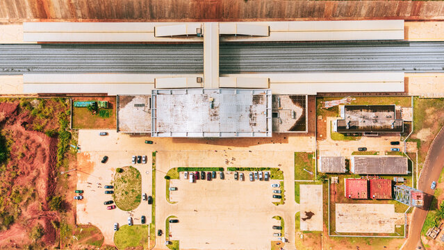 Aerial view of a modern railway station in Abeokuta, featuring a long platform, tracks, a central building, and a parking lot with cars, surrounded by red earth. Abeokuta, Ogun State, Nigeria.