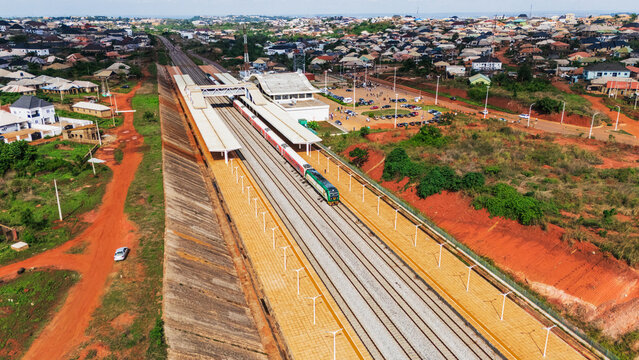 Aerial view of the modern train station with a passenger train arriving at the platform, surrounded by residential buildings and red earth landscape in Abeokuta, Ogun State, Nigeria.