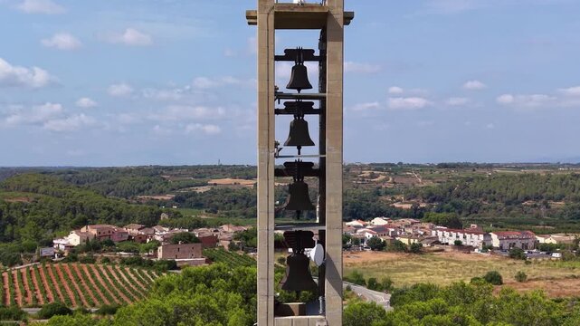 Tall minimalist concrete bell tower with vertical row of hanging bells near Santuari de Montferri, Tarragona, Catalonia, Spain, overlooking village, vineyards, and rolling countryside