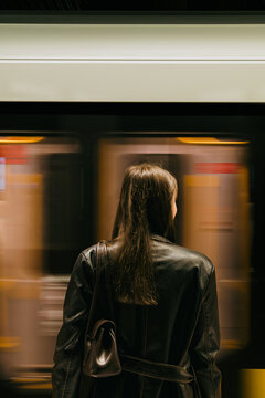 Young woman standing on an underground subway platform from behind while a fast train passes by with dynamic motion blur. Warsaw metro