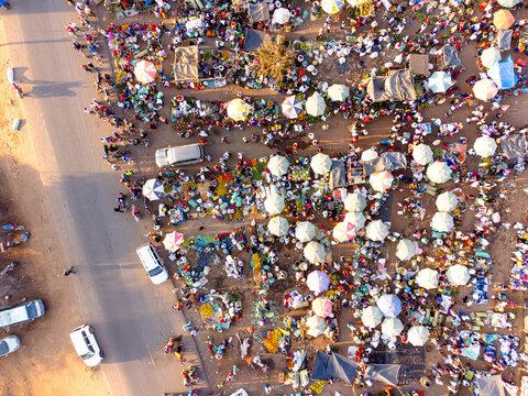 Aerial view of a bustling outdoor market with colorful umbrellas, numerous stalls, and crowds of people gathered on the dusty ground in Kimana, Kajiado County, Kenya.