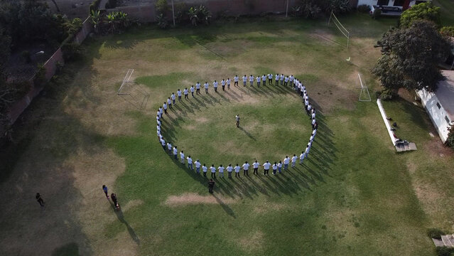 Aerial view of a large group of people forming a circle on a green grass field during a company integration event in Lima, Callao Region, Peru.