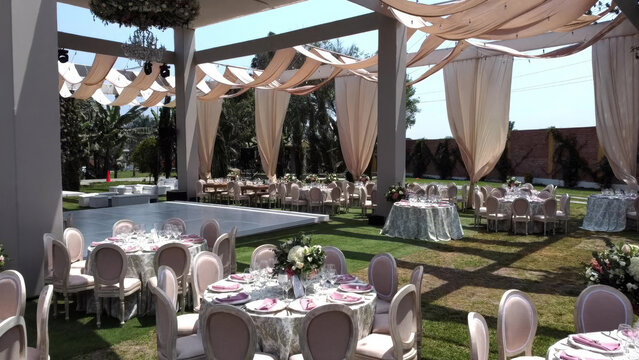 Aerial view of wedding reception setup with elegant round tables, chairs, and draped fabric ceiling decorations on a grassy lawn in Lima, Callao Region, Peru.