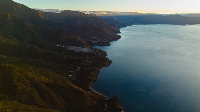Aerial view of Rostro Maya overlooking Lake Atitlan with lush mountain slopes, calm water, and distant village settlements in Santa Clara la Laguna, Solola, Guatemala.