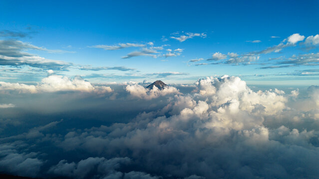 Aerial view of Acatenango volcano peak rising above a dense layer of clouds under a clear blue sky in Alotenango, Sacatepequez Department, Guatemala.