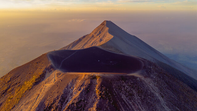 Aerial view of Acatenango volcano crater at sunset with golden light illuminating the volcanic slopes and rocky terrain in Alotenango, Sacatepequez Department, Guatemala.