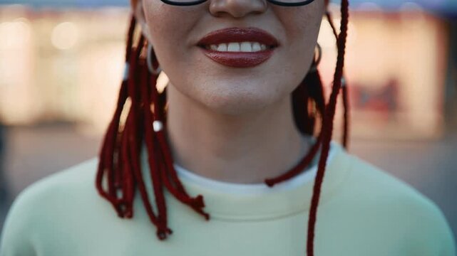 Woman with red dreadlocks and glasses smiling in urban setting