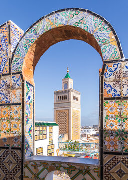 View of the minaret of the Zitouna Mosque framed by a colorful traditional tiled archway in the historic medina of Tunis, Tunis Governorate, Tunisia.