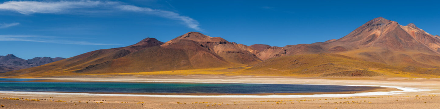View of the turquoise waters of Miscanti Lake surrounded by arid volcanic mountains and salt flats in San Pedro de Atacama, Antofagasta, Chile.