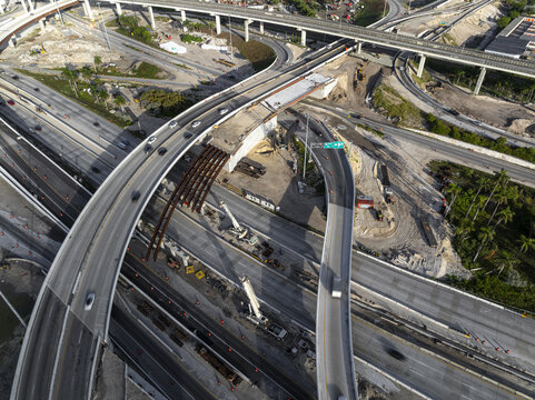 Aerial view of the Golden Glades Interchange under construction with concrete pillars, heavy machinery, and traffic on surrounding highways in Miami, Florida, United States.