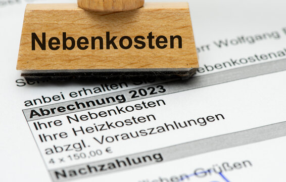 Ein Holzstempel mit Aufdruck Nebenkosten steht auf einer Nebenkostenabrechnung f&uuml;r eine Mietwohnung mit Berechnung des pers&ouml;nlichen Verbrauchs und einer Nachzahlung. - Symbolbild