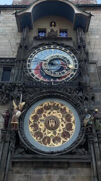frontal upward view of historic clock tower showing stacked astronomical dial with blue and red sectors above gilded medallion dial with painted circular panels