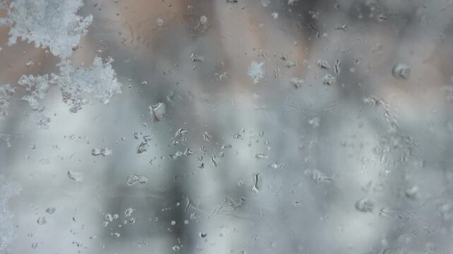 Cinematic close-up of melting snowflakes and icy raindrops on a window glass, captured with a slow shutter speed for a soft, meditative winter mood. Delicate ice crystals and water droplets 