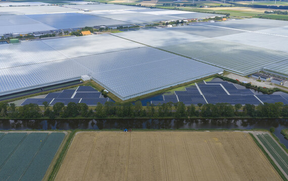 Aerial view of large-scale glass greenhouses and floating solar panels installed on a canal, surrounded by agricultural fields in the Netherlands.