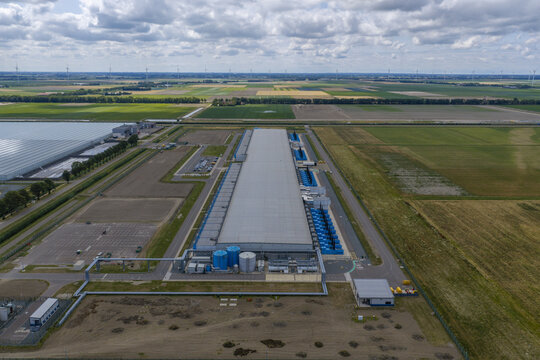 Aerial view of the Google data center facility surrounded by agricultural fields, greenhouses, and wind turbines in the Netherlands.