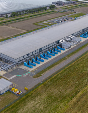 Aerial view of the Google data center facility featuring rows of blue cooling units, industrial infrastructure, and a parking lot surrounded by agricultural fields in the Netherlands.