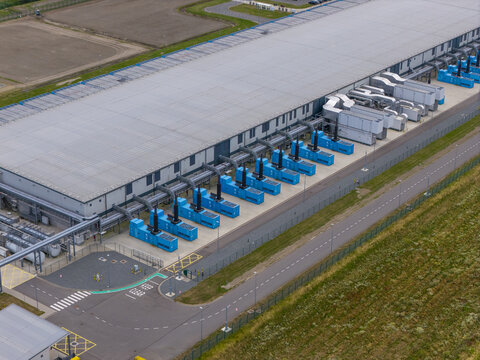 Aerial view of a large data center facility with rows of blue industrial cooling units and extensive rooftop infrastructure in the Netherlands.