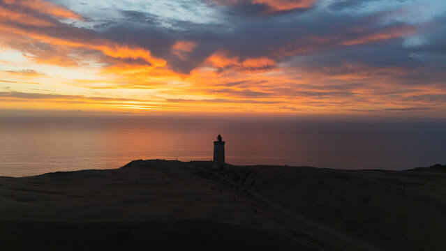Aerial view of Rubjerg Knude lighthouse standing on the sand dunes against a vibrant sunset sky over the North Sea in Lokken, Denmark.