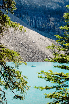 View of Moraine Lake with a canoe on the turquoise water, framed by pine trees and a steep rocky mountainside in Improvement District No. 9, Alberta, Canada.