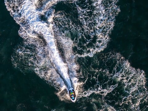 Aerial view of a jet ski cutting through the dark blue ocean water, leaving a white wake behind in Cascais, Lisboa, Portugal.