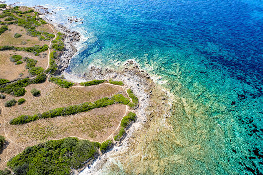 Aerial view of Plage de Ghjunchitu with its turquoise waters, rocky coastline, and winding trails through the Mediterranean scrubland in Corbara, Corse, France.