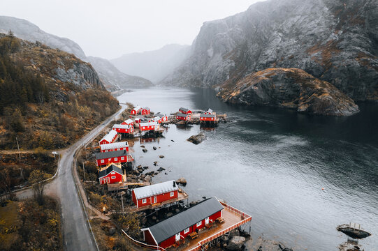 Aerial view of the historic fishing village of Nusfjord with its iconic red wooden cabins built on stilts along the rocky shoreline of the fjord in Nusfjord, Nordland, Norway.