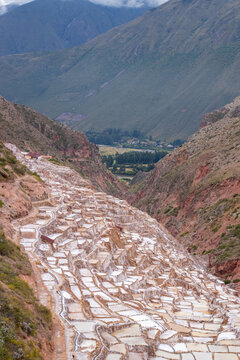 View of the historic Maras Salt Mines with numerous white salt evaporation ponds terraced into the steep mountain valley in Cusco, Cusco, Peru.
