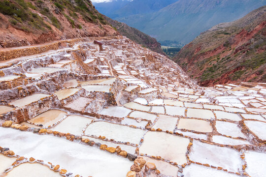View of the historic Maras Salt Mines with terraced salt evaporation ponds carved into the hillside, surrounded by rugged Andean mountains in Cusco, Cusco, Peru.