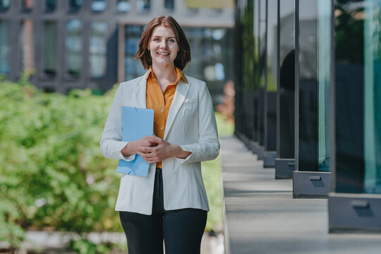 A smiling businesswoman holds a folder outdoors at the office