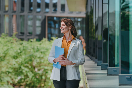 Smiling businesswoman holds a blue folder outside the office