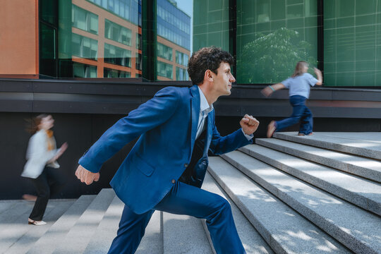 A businessman in a blue suit runs up outdoor stairs in a rush