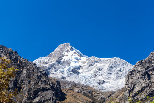View of the snow-capped peak of a mountain in the Andes with rocky slopes under a clear blue sky in Ancash, Peru.