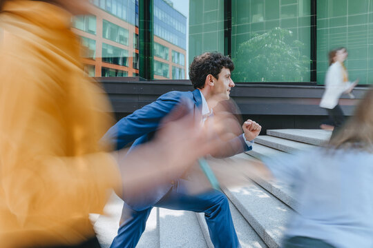 Businessman runs up stairs outdoors among blurred business people