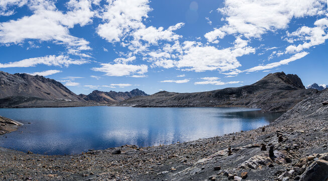View of a high-altitude mountain lake surrounded by rocky peaks and a vast blue sky in the Andes mountains, Ancash, Peru.