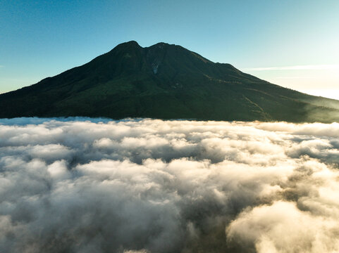 Aerial view of Gunung Mongkrang rising above a thick sea of clouds during the golden hour in Jatiyoso, Central Java, Indonesia.