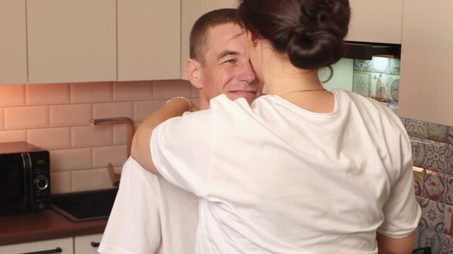 Beautiful young couple spending cozy moments together while talking in the kitchen. Their genuine smiles and relaxed atmosphere symbolize romance, closeness, and shared happiness. Back view