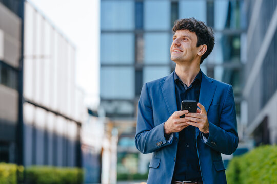 Smiling businessman holds a phone outdoors in the city