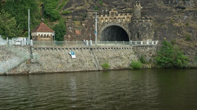 Historic Vysehrad stone tunnel portal stands built into a rocky cliff along Vltava River in Prague. The scenic embankment represents Czech travel destination and transport infrastructure.