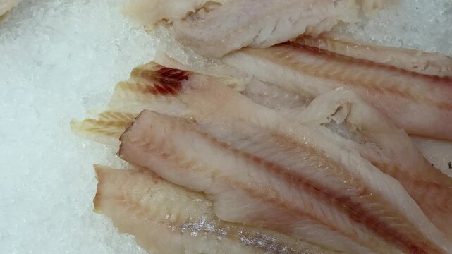Thawed cod fillet on ice stacked on shallow crushed ice at supermarket counter, pale flesh glistening with visible moisture