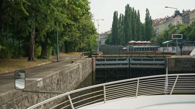An excursion boat approaches closed metal gates of the Smichov canal lock in Prague on the Vltava River. Scenic river cruise showcases urban transport, navigation and European travel.